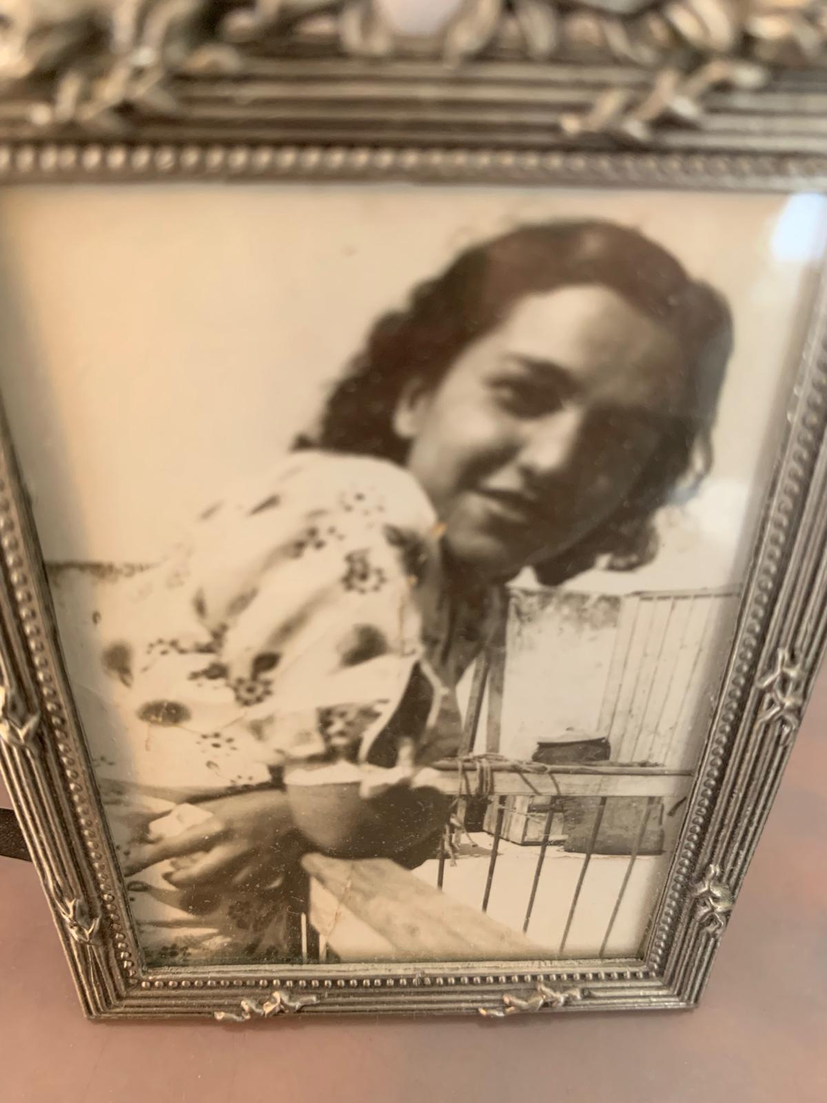**Messody née Lévy, épouse Assouline**. La maman de Mamie, l'arrière-grand-mère d'Aaron. Portrait jeune dans un cadre argenté, robe à motifs floraux, accoudée à une rambarde de balcon. Confirmé par Mamie elle-même.
